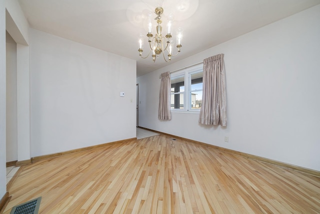 empty room with wood-type flooring, visible vents, a notable chandelier, and baseboards