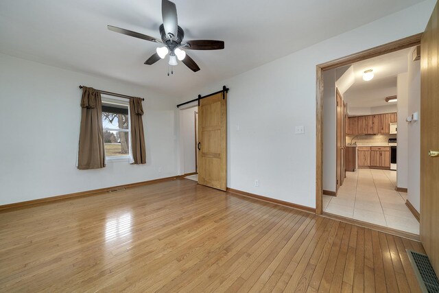 unfurnished bedroom featuring visible vents, light wood-style flooring, baseboards, and a barn door