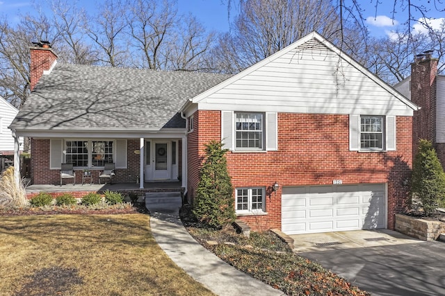 split level home featuring brick siding, a chimney, a porch, an attached garage, and driveway