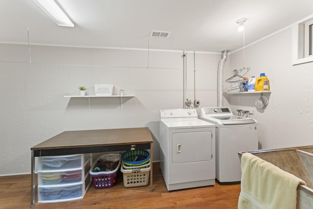 laundry room with laundry area, separate washer and dryer, wood finished floors, visible vents, and crown molding