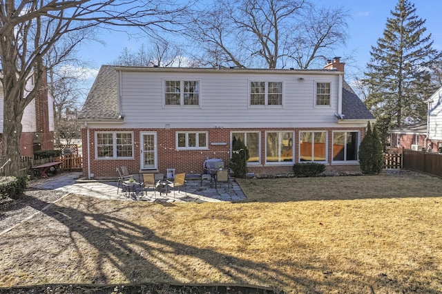 rear view of property featuring brick siding, a chimney, a lawn, a patio area, and fence