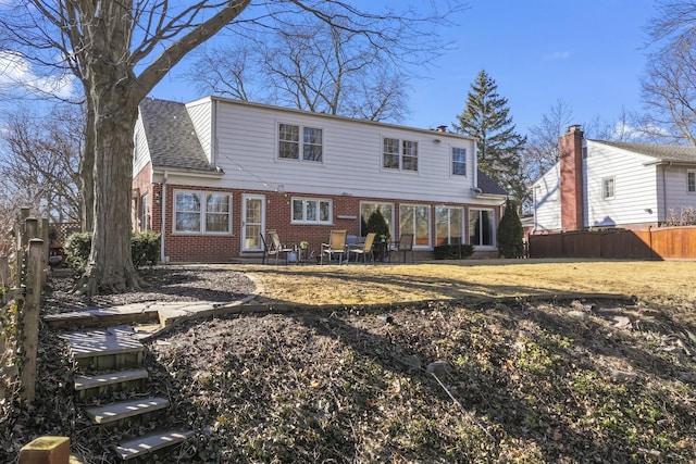 view of front facade featuring brick siding, fence, and roof with shingles