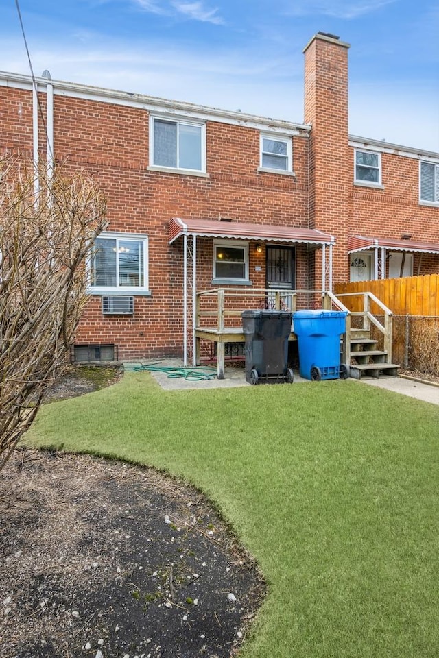 rear view of property featuring a yard, brick siding, a chimney, and fence