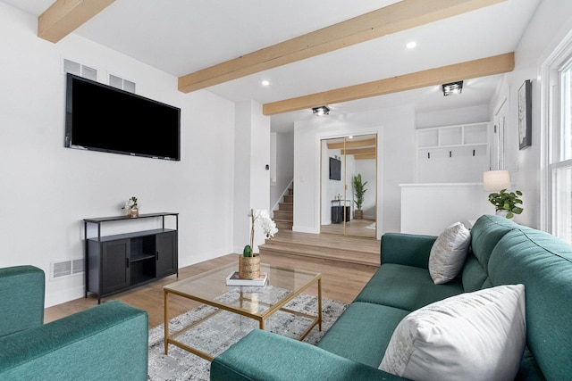 living area featuring stairway, visible vents, beam ceiling, and wood finished floors