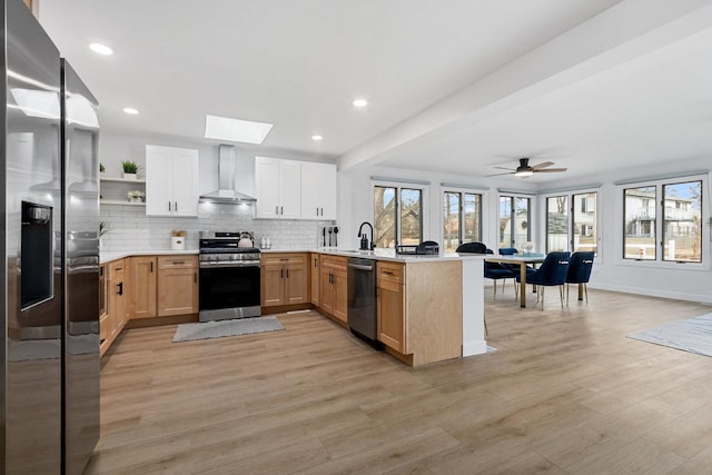 kitchen featuring a peninsula, appliances with stainless steel finishes, wall chimney range hood, backsplash, and open shelves