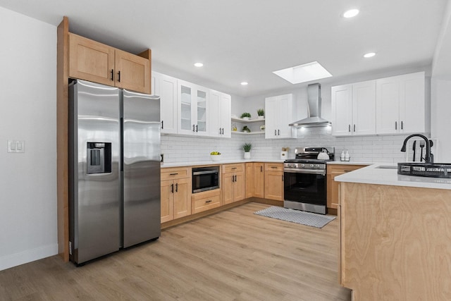 kitchen featuring stainless steel appliances, a sink, wall chimney range hood, and light wood finished floors