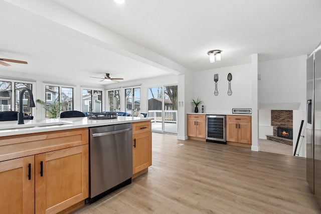 kitchen with light wood-style floors, a brick fireplace, a sink, beverage cooler, and dishwasher