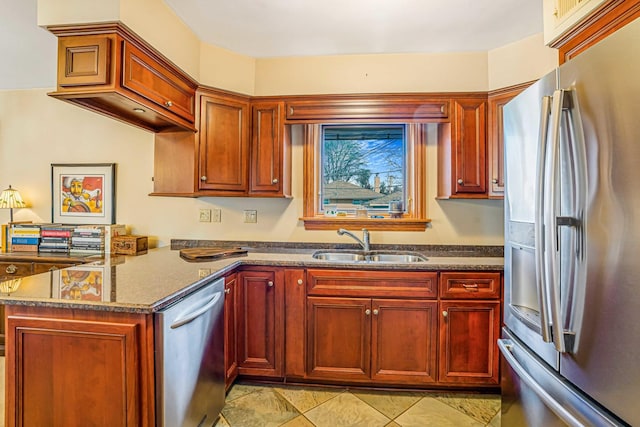 kitchen with dark stone counters, reddish brown cabinets, appliances with stainless steel finishes, and a sink