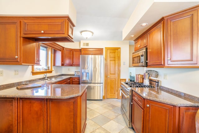 kitchen with visible vents, brown cabinets, appliances with stainless steel finishes, a peninsula, and stone countertops