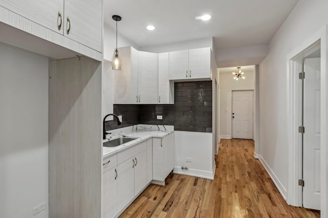 kitchen with light wood-style flooring, a sink, white cabinets, light countertops, and tasteful backsplash