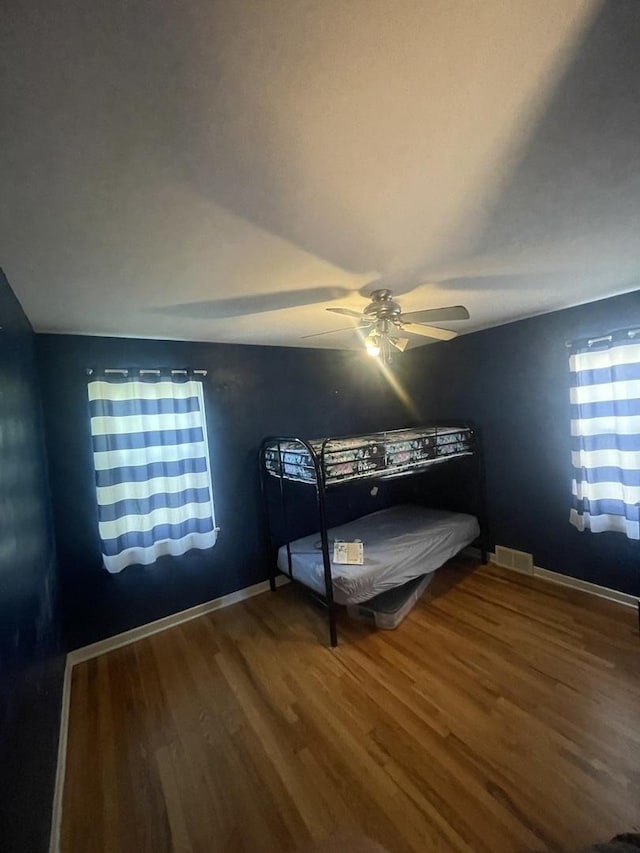 unfurnished bedroom with a ceiling fan, wood finished floors, visible vents, and baseboards