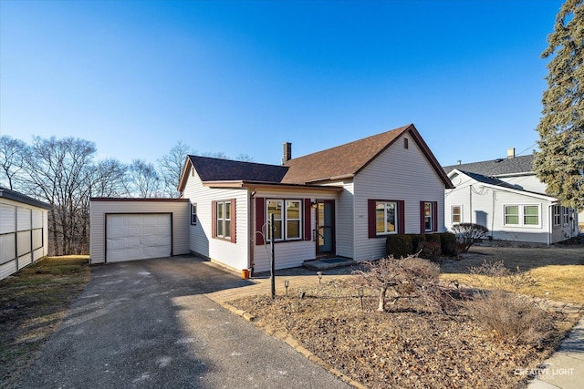 view of front of house with driveway, a garage, a chimney, and an outbuilding