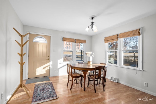 dining room with light wood finished floors, baseboards, visible vents, and a notable chandelier