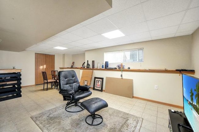 living area featuring a drop ceiling and baseboards