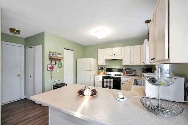 kitchen with a peninsula, light countertops, freestanding refrigerator, dark wood-style floors, and gas stove