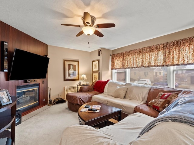 living area with a fireplace, light carpet, ceiling fan, wooden walls, and a textured ceiling