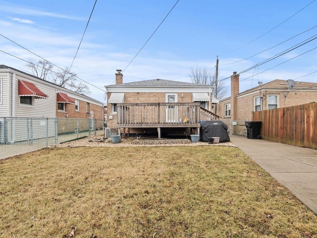 rear view of house with a deck, a fenced backyard, brick siding, a lawn, and a chimney