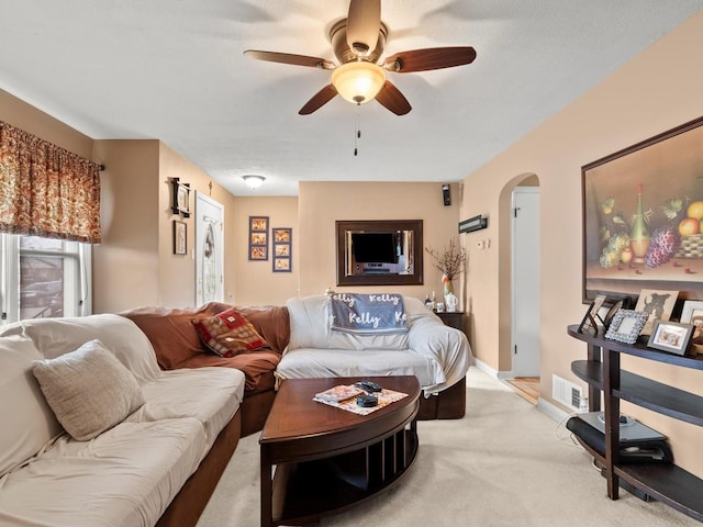 living room featuring arched walkways, light colored carpet, a ceiling fan, baseboards, and visible vents