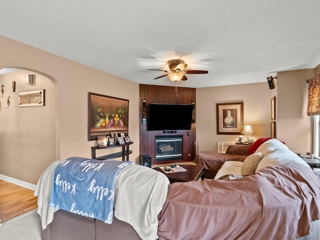 living room featuring a large fireplace, arched walkways, baseboards, ceiling fan, and wood finished floors