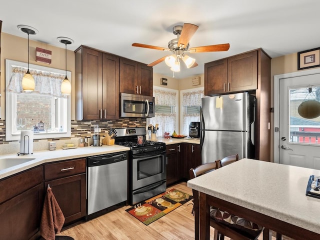 kitchen featuring dark brown cabinetry, appliances with stainless steel finishes, light countertops, light wood-style floors, and backsplash