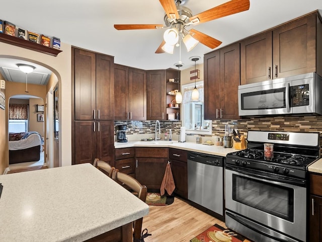 kitchen featuring arched walkways, open shelves, light countertops, appliances with stainless steel finishes, and a sink