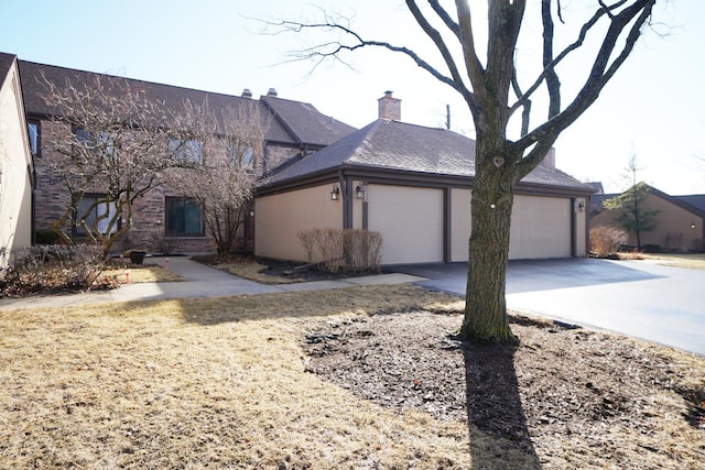 view of front of property featuring a garage, a shingled roof, brick siding, concrete driveway, and a chimney