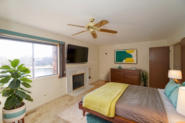 bedroom with a high end fireplace, visible vents, ceiling fan, and light carpet