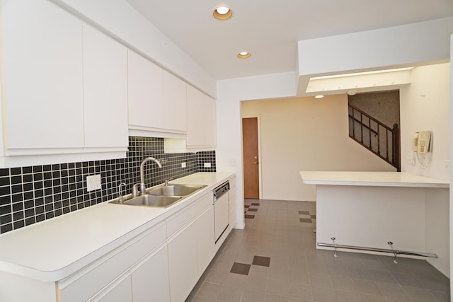 kitchen featuring tasteful backsplash, white dishwasher, light countertops, white cabinetry, and a sink