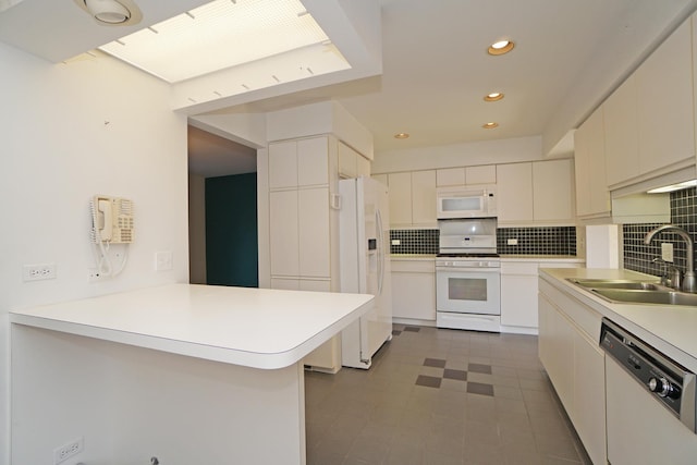 kitchen with a peninsula, white appliances, backsplash, and a sink