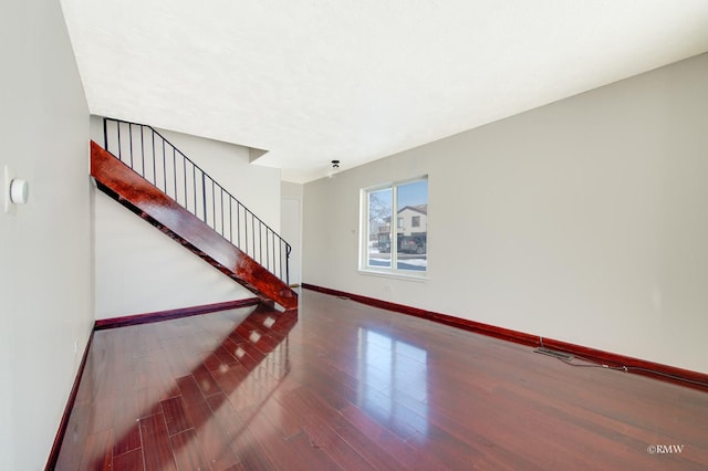 unfurnished living room with wood finished floors, baseboards, and stairs