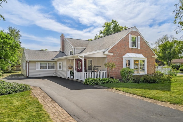 view of front of home featuring a chimney, aphalt driveway, covered porch, a front yard, and brick siding