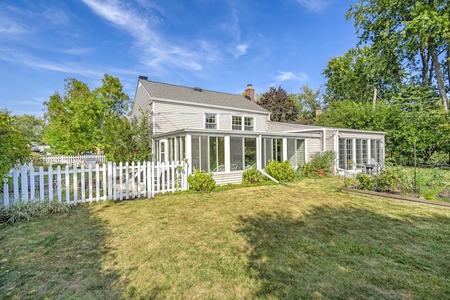 rear view of house featuring a yard, a chimney, a sunroom, fence, and a garden