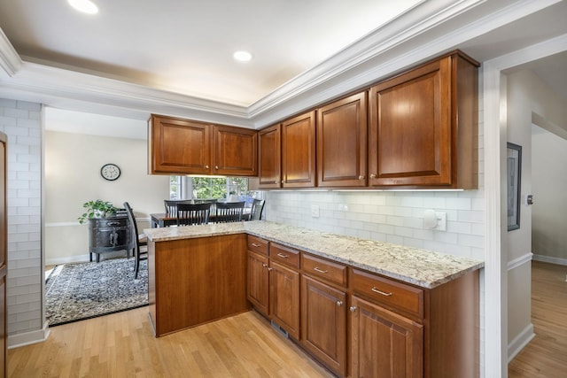 kitchen featuring a peninsula, light stone countertops, and light wood-style floors