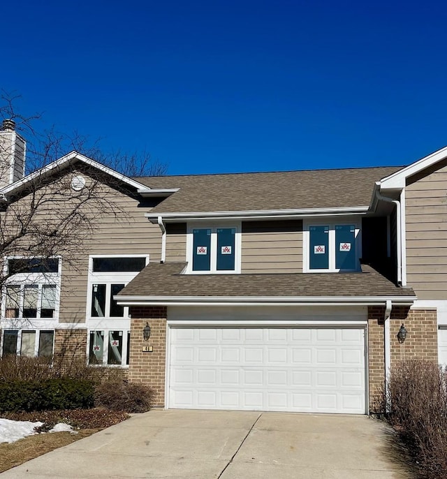 view of front of home with driveway, an attached garage, a chimney, and brick siding