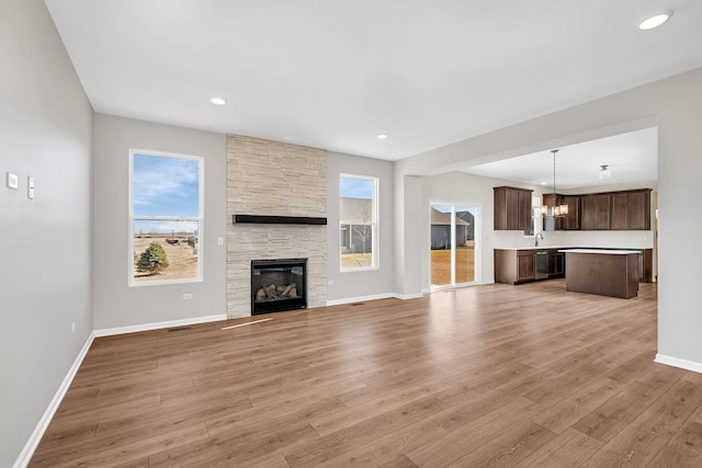 733 Juniper St, Oswego, IL 60543 - unfurnished living room with a chandelier, light wood-type flooring, a stone fireplace, and recessed lighting