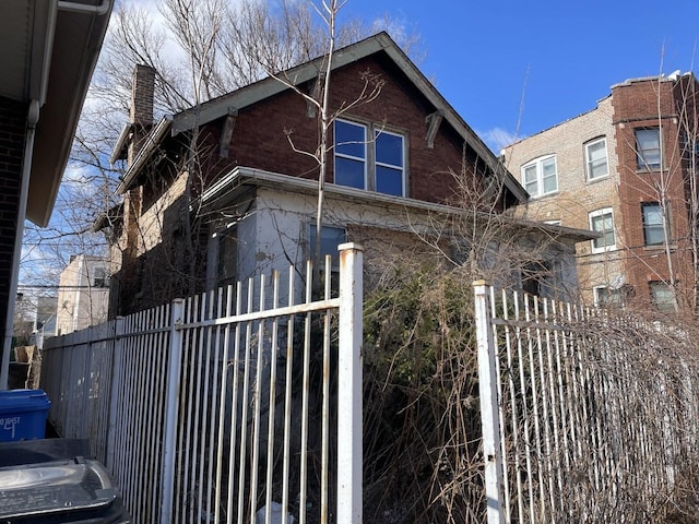 view of side of home featuring a chimney, fence, and brick siding