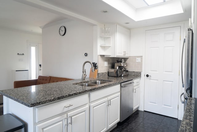 kitchen featuring stainless steel appliances, a peninsula, a sink, white cabinetry, and decorative backsplash