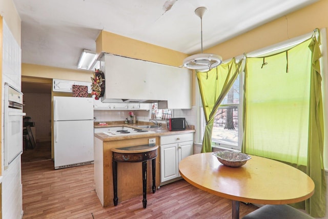 kitchen with white appliances, white cabinetry, a sink, and light wood finished floors