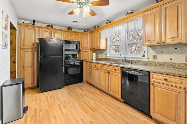 kitchen featuring light wood finished floors, tasteful backsplash, light stone counters, black appliances, and a sink