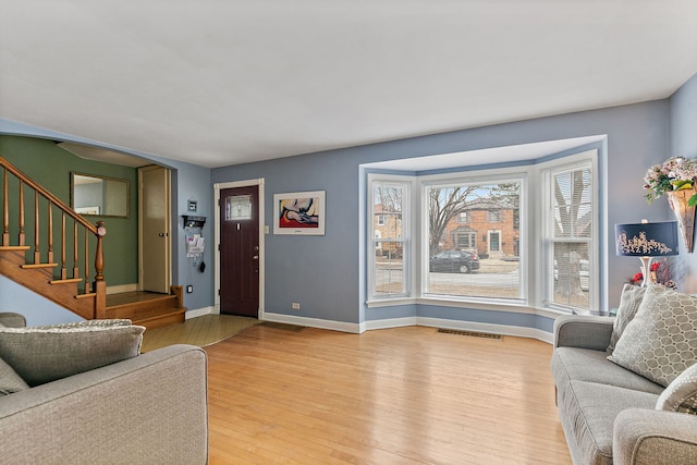 living area with light wood-type flooring, visible vents, baseboards, and stairs