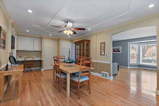 dining room with light wood-type flooring, baseboards, built in desk, and ornamental molding