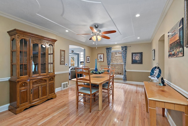 dining room with arched walkways, visible vents, baseboards, ornamental molding, and light wood-type flooring