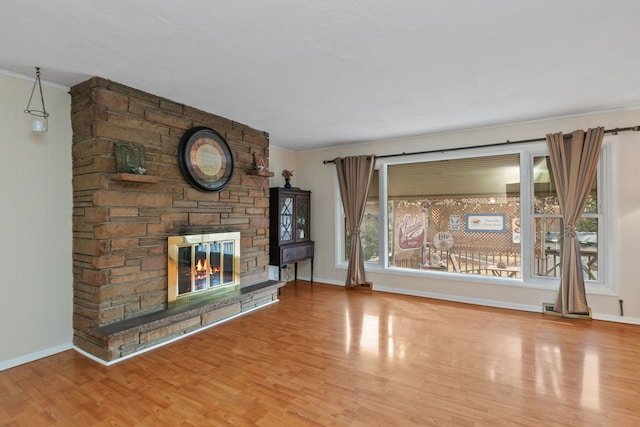 unfurnished living room with ornamental molding, a stone fireplace, baseboards, and wood finished floors