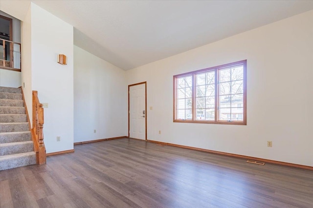 empty room with baseboards, visible vents, lofted ceiling, stairway, and wood finished floors