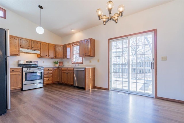 kitchen with under cabinet range hood, stainless steel appliances, vaulted ceiling, light countertops, and dark wood finished floors