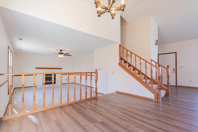 interior space with baseboards, wood finished floors, a high ceiling, stairs, and ceiling fan with notable chandelier