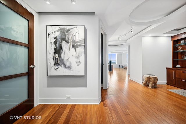 hall with wood-type flooring, rail lighting, and baseboards