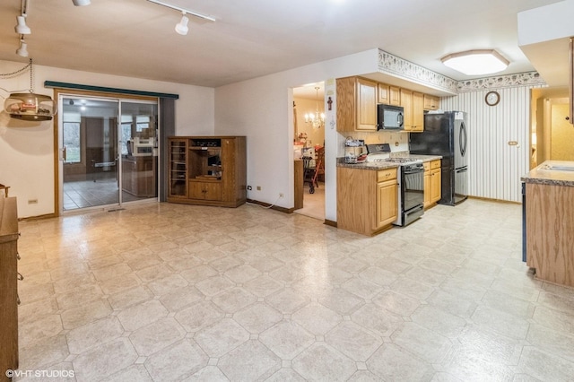 kitchen featuring black microwave, baseboards, range with gas stovetop, freestanding refrigerator, and light floors