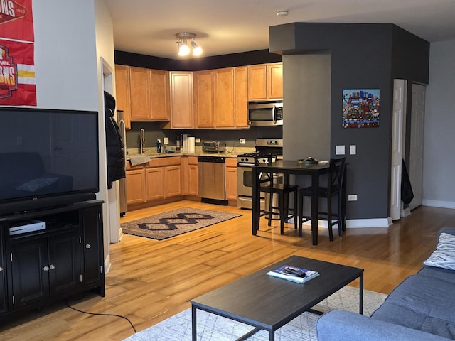 kitchen featuring light wood finished floors, light countertops, appliances with stainless steel finishes, light brown cabinets, and baseboards