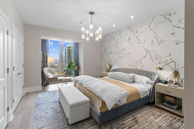 bedroom with baseboards, an accent wall, wood finished floors, access to exterior, and an inviting chandelier